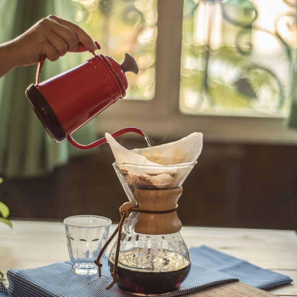 A barista pouring a V60 pour-over from a copper gooseneck kettle.