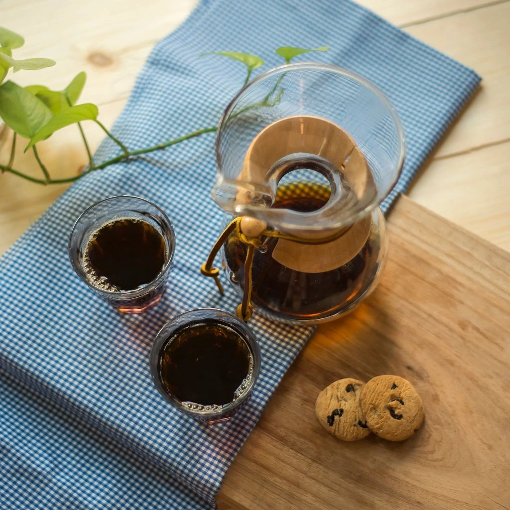 A glass carafe of batch-brew coffee with a printed origin card.